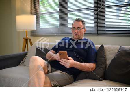 Senior man relaxing on sofa and using smartphone at home Senior man relaxing on sofa and using smartphone at home 126626147