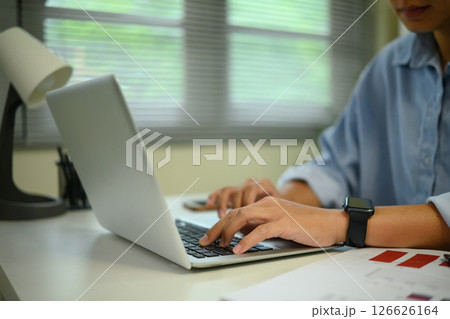 Close up of hands typing on a laptop in a bright home office with modern decor Close up of hands typing on a laptop in a bright home office with modern decor 126626164