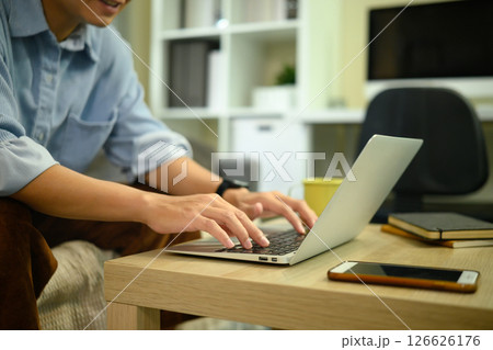 Close up of man working on laptop at home, focusing on hands typing on keyboard 126626176