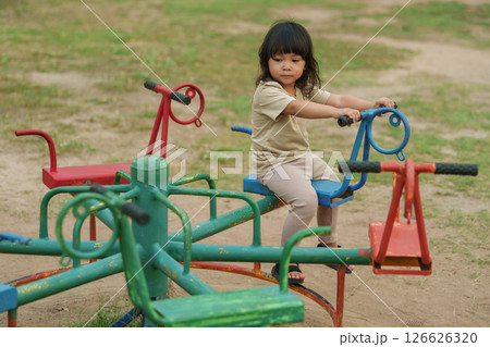 toddler girl having fun while playing on carousel at playground toddler girl having fun while playing on carousel at playground 126626320