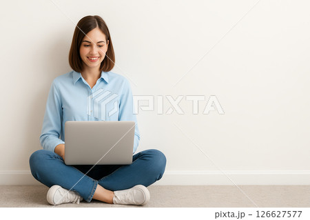 Young caucasian woman smiling while using a laptop on the floor against a minimalist white background. concept of comfortable online work, casual home style, technology interaction, copy space. 126627577