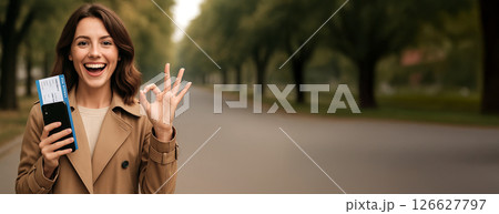 Cheerful caucasian woman holding ticket on tree-lined street. concept of travel excitement, outdoor adventure, joyful journey, exploring new destinations, Copy space, Wide banner 126627797