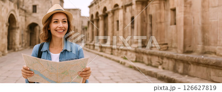 Smiling caucasian female tourist holding a map in a sunlit ancient city. concept of travel exploration, joyful adventure, cultural journey, historic sightseeing, Copy space. Wide Banner 126627819