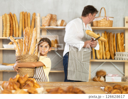 Girl daddy assistant poses in bakery with baguettes of bread Girl daddy assistant poses in bakery with baguettes of bread 126628617