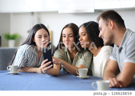 Interracial friends checking mobile phone content in a kitchen Interracial friends checking mobile phone content in a kitchen 126628659