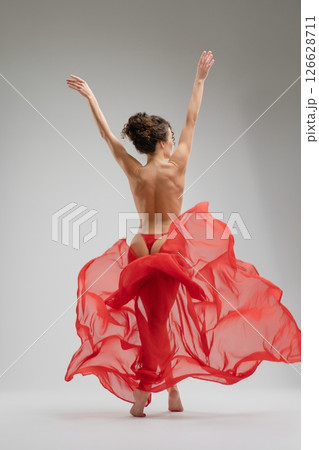 Expressive nude ballet dancer gracefully moving in flowing red fabric 126628711
