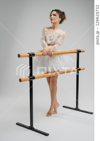 Elegant ballet dancer poses gracefully near a barre under soft lighting Elegant ballet dancer poses gracefully near a barre under soft lighting 126628732