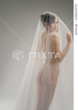 Elegant woman draped in a sheer veil poses gracefully in a minimalist setting Elegant woman draped in a sheer veil poses gracefully in a minimalist setting 126628752