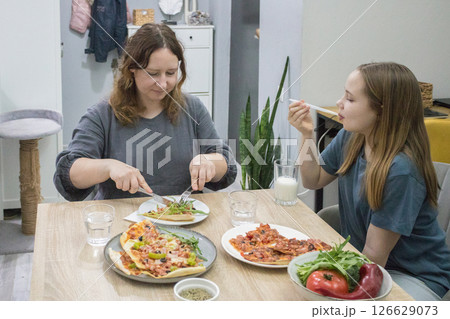 Mother and daughter eating homemade pizza for dinner at home 126629073