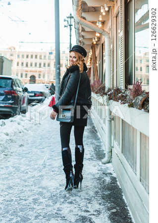 Pretty brunette woman in black leather jacket and high heels standing 126629302