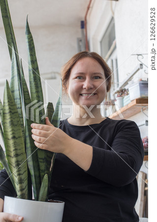 Happy mid adult woman holding green houseplant in her hand standing indoor. Happy mid adult woman holding green houseplant in her hand standing indoor. 126629528