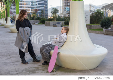 Family together. Mother and daughter with skateboard resting outdoors Family together. Mother and daughter with skateboard resting outdoors 126629860