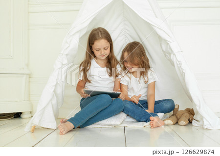 Adorable little girl sisters with tablet pc computer in kids tent at home. Adorable little girl sisters with tablet pc computer in kids tent at home. 126629874