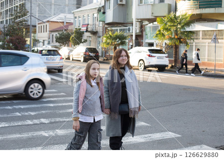 Pretty mother and daughter hold each other's hand and cross the road at a crosswalk Pretty mother and daughter hold each other's hand and cross the road at a crosswalk 126629880