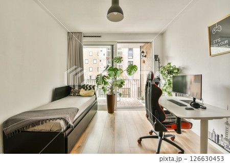 A stylish and minimalistic home office featuring a desk, chair, and plant, complemented by a view of the balcony through large glass doors. Perfect for work or relaxation. A stylish and minimalistic home office featuring a desk, chair, and plant, complemented by a view of the balcony through large glass doors. Perfect for work or relaxation. 126630453