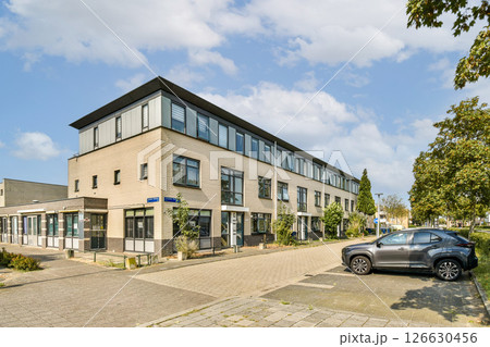 A contemporary building with a sleek design, located on a street lined with trees and greenery, showcasing a blend of urban architecture and nature. 126630456