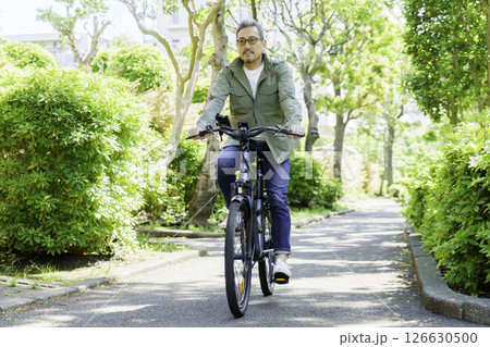 新緑の中、電動機付き自転車に乗るミドルエイジの男性 新緑の中、電動機付き自転車に乗るミドルエイジの男性 126630500