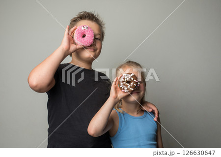 Pretty sister and brother having fun holding donuts standing against white wall. Pretty sister and brother having fun holding donuts standing against white wall. 126630647
