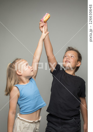 Young sister and brother having fun holding donuts standing against white background wall.  126630648