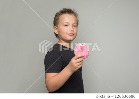 Handsome child boy holding testy donut. Kid in black t-shirt with sweet food indoor Handsome child boy holding testy donut. Kid in black t-shirt with sweet food indoor 126630686