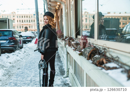 Beautiful happy brunette woman in black leather jacket and black hat holding light blue handbag 126630710