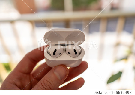 A man holds a pair of wireless earphones in an open white charging case. A man holds a pair of wireless earphones in an open white charging case. 126632498