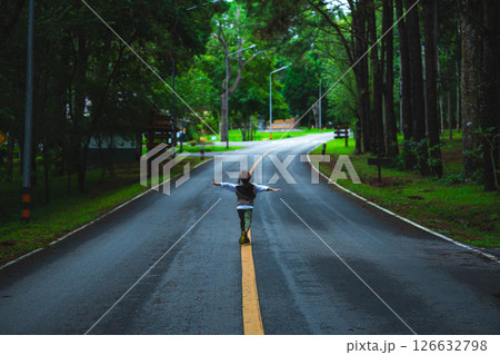 Happy little girl tourist walking on asphalt road outdoors enjoying beautiful nature of forest in national park on spring vacation. Happy little girl tourist walking on asphalt road outdoors enjoying beautiful nature of forest in national park on spring vacation. 126632798