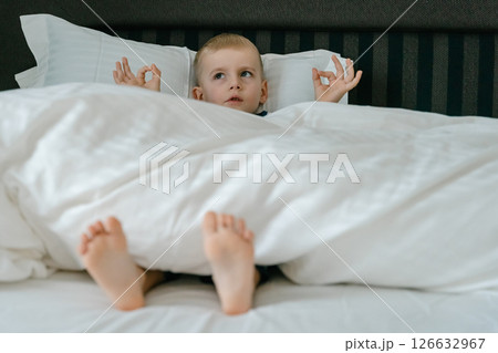 a little blond-haired boy in blue pajamas in his parents' bed lounging in the white sheets. High quality photo 126632967