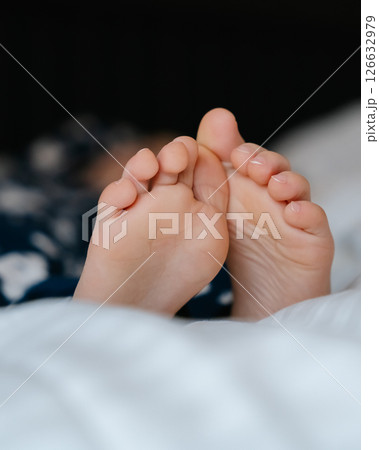 The feet of a small child in a parent's bed on white sheets rolled in a white blanket . High quality photo 126632979