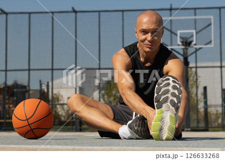 Happy Basketball player stretching legs after game. Outdoors summer training. Healthy and sport lifestyle concept. Happy Basketball player stretching legs after game. Outdoors summer training. Healthy and sport lifestyle concept. 126633268