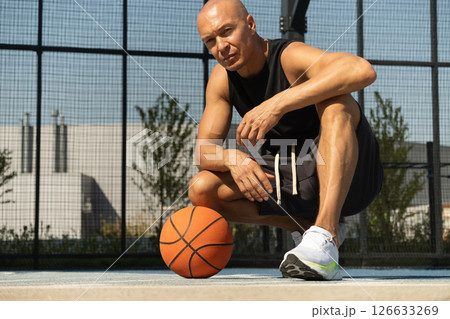 Basketball player sits and relax after workout at sport stadium. Professional athlete or sportsman with accident. Outdoor. Sport leisure activity. 126633269