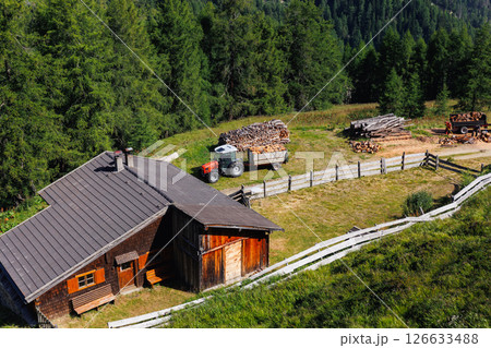 Scenic aerial view alpine village log wooden countryside cabin lumber stock lumber timber manufacture yard tractor machinery and storage. Rural landscape meadow wood piles forestry country vibe 126633488