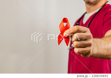 Healthcare professional holds red ribbon symbolizing HIV awareness in clinic 126634691