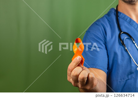 Healthcare professional holding orange and yellow awareness ribbon indoors Healthcare professional holding orange and yellow awareness ribbon indoors 126634714
