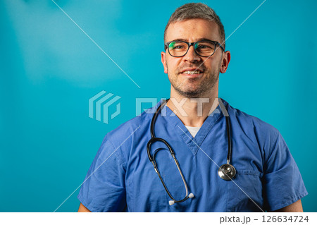 Healthcare professional in blue scrubs smiles against a vibrant background Healthcare professional in blue scrubs smiles against a vibrant background 126634724