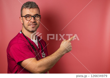 Medical professional in scrubs pointing to a blank wall background Medical professional in scrubs pointing to a blank wall background 126634979
