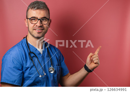 Doctor in scrubs gestures towards a blank space with a friendly smile 126634991