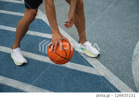 Basketball player dribbling ball, capturing motion and shadow on blue outdoor court. Basketball player dribbling ball, capturing motion and shadow on blue outdoor court. 126635131