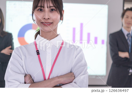 会議室のスクリーンの前で腕組しながら立つ男女 126636497