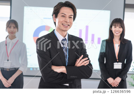 会議室のスクリーンの前で腕組しながら立つ男女 126636596