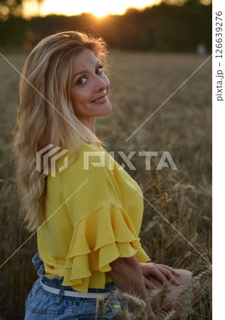 Woman stands in a golden field of wheat during sunset, showcasing natural beauty and serenity in a rural setting 126639276