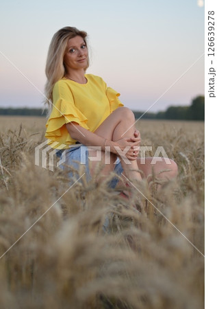 Woman stands in a golden field of wheat during sunset, showcasing natural beauty and serenity in a rural setting 126639278