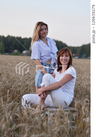 Two women enjoying a joyful moment in a golden wheat field during sunset while wearing bright summer outfits in a rural setting Two women enjoying a joyful moment in a golden wheat field during sunset while wearing bright summer outfits in a rural setting 126639279