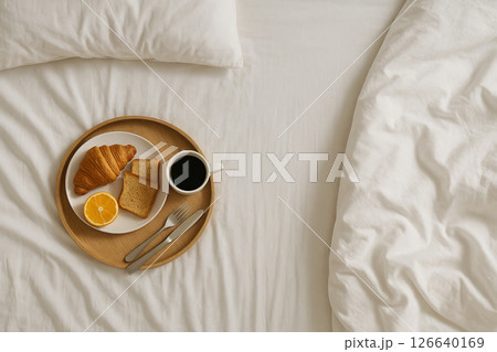 Breakfast in bed with coffee, croissant, toast, and orange slice on wooden tray - cozy morning routine and relaxation concept, Copy space 126640169