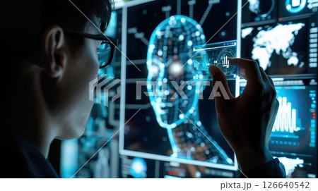 A young Asian man with glasses interacts with a digital interface displaying a holographic human head and data graphs. The scene represents future technologies and artificial intelligence. 126640542