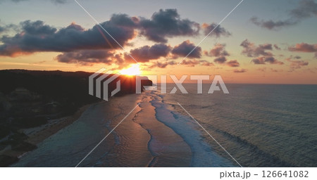 Golden sunset illuminating breaking ocean waves on a beautiful beach on the coast of Bali, Indonesia, with cliffs and colorful clouds creating a breathtaking view 126641082