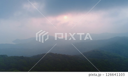 Layers of misty mountains and forest fading into the distance as the sun sets behind a cloudy sky, creating a serene and atmospheric landscape Layers of misty mountains and forest fading into the distance as the sun sets behind a cloudy sky, creating a serene and atmospheric landscape 126641103