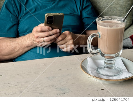 an elderly man holds a phone in his hands in a cafe, there is a fragrant latte on the table. High quality photo an elderly man holds a phone in his hands in a cafe, there is a fragrant latte on the table. High quality photo 126641704
