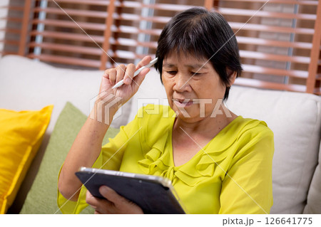 Senior asian woman sitting on sofa using digital tablet with relax in living room at home. Senior asian woman sitting on sofa using digital tablet with relax in living room at home. 126641775