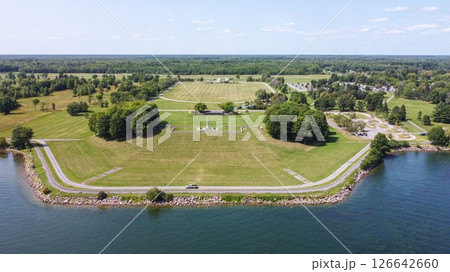 Aerial view of a lakeside park with a large grassy area, a monument, and a road along the water. 126642660